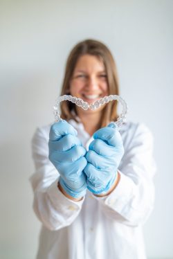 Dentist holding invisible braces aligner, showing heart shape, orthodontic treatment